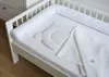 A white baby crib with a white bumper and a white blanket and pillow. Produktbild-Vorschau