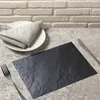 A table setting with a slate-look placemat, a white plate with a folded gray napkin, a fork, and a knife. Anteprima dell’immagine prodotto