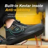 A close-up shot of a person's foot wearing a black work shoe, with orange and blue accents. The shoe is positioned on a wooden surface with several orange spikes protruding from it, demonstrating the shoe's anti-stabbing feature. Text overlays highlight th Produktbild-Vorschau