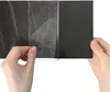 Hands peeling a protective film off a black vinyl flooring tile. Produktbild-Vorschau
