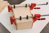 A wooden box being held together by two red clamps on a white table. Produktbild-Vorschau