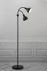 A black floor lamp with two adjustable heads stands against a light gray wall with decorative paneling. Náhled obrázku produktu