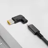 A laptop adapter and a USB-C cable are shown on a light gray surface, with a portion of a laptop visible in the foreground. Náhled obrázku produktu