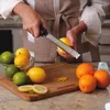 A person is zesting a lemon over a cutting board with other citrus fruits nearby. Anteprima dell’immagine prodotto