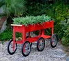 A red planter cart filled with green plants sits on a gravel path in a garden. Produktbild-Vorschau