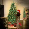 A young girl in a Santa hat stands in front of a decorated Christmas tree, with presents underneath. A mirror reflects another girl and tree. Produktbild-Vorschau