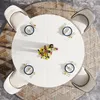 A round white dining table set for four people with a floral centerpiece, viewed from directly above. Náhled obrázku produktu