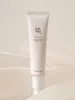 A light pink tube of eye serum is centered on a white and light gray background with soft fabric folds. Voir les images du produit