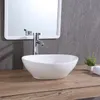 A white oval washbasin with a chrome faucet is shown on a wooden countertop, with a mirror and a small plant in the background. Produktbild-Vorschau