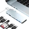 A silver USB-C hub is shown connected to a laptop, with various cables and memory cards arranged around it. Produktbild-Vorschau