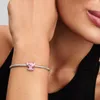 A close-up shot of a woman's arm wearing a silver bracelet with a pink Stitch charm. Podgląd zdjęcia produktu