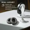 A pair of replacement ear pads for headphones are shown on a white surface next to a pair of headphones on a stand and a small white cup. Produktbild-Vorschau