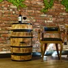 A wine barrel table with a bottle of wine and a glass on top, next to a wooden chair in front of a brick wall. Náhled obrázku produktu