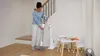 A woman is using a cordless vacuum cleaner in a home setting near stairs and a children's table. Anteprima dell’immagine prodotto