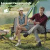 A couple sitting on a loveseat camping chair next to a lake with a tent in the background. Produktbild-Vorschau