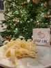 A pile of fresh pasta sits on a plate in front of a decorated Christmas tree. A box with a logo and text is also visible. Produktbild-Vorschau
