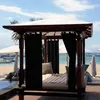 A cabana with black curtains on a beach with umbrellas and boats in the background. Náhled obrázku produktu