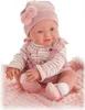 A baby doll dressed in pink clothing, sitting on a pink blanket. Anteprima dell’immagine prodotto