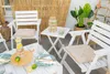 An outdoor patio setting with white wooden furniture, plants, and drinks. Náhled obrázku produktu