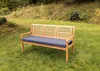 A wooden bench with a dark blue cushion sits on a grassy lawn in a garden setting. Náhled obrázku produktu