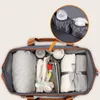 An open diaper bag filled with baby items, with a close-up inset showing bottle holders. Náhľad obrázku produktu
