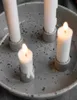 Close-up of a speckled gray ceramic candle holder with four white candles, two of which are lit. Produktbild-Vorschau