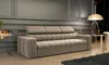 A beige sofa with a tufted design and adjustable headrests is shown in a well-lit room with paneled walls and wooden flooring.