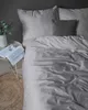 A bed with gray striped bedding, a dark gray pillow, a book, and a glass of water on a side table. Produktbild-Vorschau