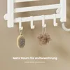 A close-up view of a white electric towel warmer with hooks, displaying a bath brush and a loofah hanging from the hooks. Text overlays highlight storage space. Anteprima dell’immagine prodotto