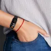 A person wearing a black fitness tracker and a red string bracelet on their wrist. Produktbild-Vorschau