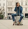 A woman sits on a suitcase in a city square. Produktbild-Vorschau
