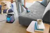 A person is cleaning a sofa with a carpet cleaner while a dog watches. Podgląd zdjęcia produktu