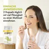 A woman is holding a pill and a glass of water, with a bottle of Gingerfit Premium on a wooden stand. Produktbild-Vorschau