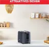 A dark gray Tefal toaster sits on a white countertop, with a woven light fixture above and shelves with various items in the background. Produktbild-Vorschau