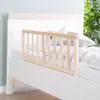 A close-up view of a white bed with a natural wood safety rail attached to the side. Produktbild-Vorschau