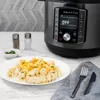 An Instant Pot Duo Crisp Multikocher is shown next to a plate of food, with salt and pepper shakers and cutlery. Produktbild-Vorschau