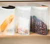 Three clear plastic food storage containers with lids are lined up on a shelf. The containers hold spaghetti, a bag of small grains, and chocolate cereal. Produktbild-Vorschau