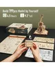 A wooden 3D model of a cello is being assembled on a dark surface, with various wooden pieces and instructions laid out. Náhľad obrázku produktu