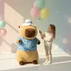 A young girl holding balloons next to a large capybara plush toy. Produktbild-Vorschau