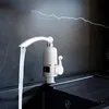 A white electric water heater faucet is installed over a black sink, with water flowing from the faucet. Náhled obrázku produktu