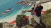 Two people are on a cliff overlooking a body of water with several boats docked. Náhľad obrázku produktu