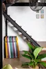 A collection of colorful folding chairs is neatly stacked against a white brick wall next to a staircase. A large green plant is in the foreground. Produktbild-Vorschau