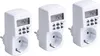 Three white digital timers with electrical outlets are arranged diagonally against a white background. Produktbild-Vorschau