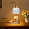 A candle warmer lamp with a Christmas-themed candle on a wooden base, placed on a desk next to books and a vase of flowers. Náhled obrázku produktu