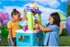 Two young girls are playing with a colorful toy ice cream cart in an outdoor setting with a whimsical, cartoonish background. Náhľad obrázku produktu