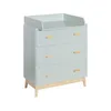 A light green changing table with wooden accents and three drawers, shown from a three-quarter angle against a white background. Podgląd zdjęcia produktu
