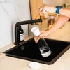 A person is filling a glass with water from a faucet into a sink. Produktbild-Vorschau