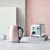 A pink kettle and a mint green toaster are displayed on a surface with a light gray and pink background. Voir les images du produit