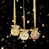 Three perfume bottles hanging with gold ribbons against a black background with gold bokeh lights. Voir les images du produit