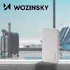 A white power bank sits on a counter in front of a blurred airport scene with luggage and airplane visible through the window. Náhľad obrázku produktu